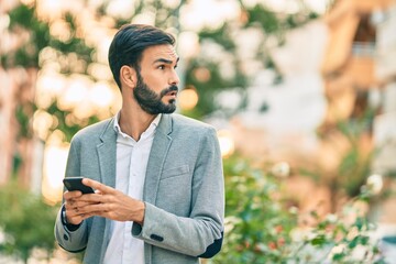 Young hispanic businessman with serious expression using smartphone at the city.