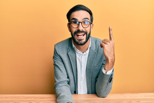 Young hispanic man working at the office pointing finger up with successful idea. exited and happy. number one.