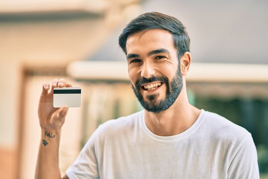 Young hispanic man smiling happy holding credit card at the city.