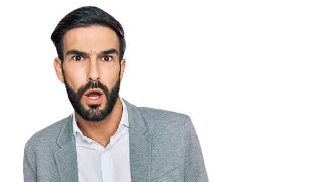 Young hispanic man wearing business clothes in shock face, looking skeptical and sarcastic, surprised with open mouth