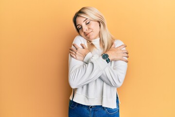 Young caucasian woman wearing casual winter sweater hugging oneself happy and positive, smiling confident. self love and self care