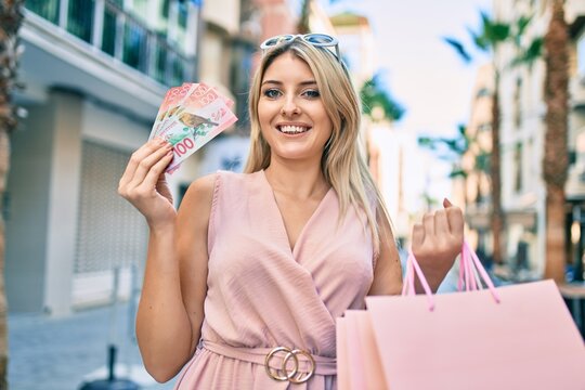 Young blonde woman smiling happy holding shopping bags and new zealand dollars at the city.