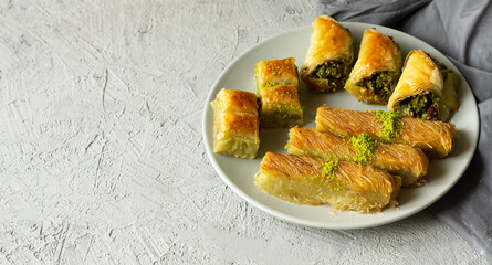 Traditional turkish various pistachio baklava and burma kadayif in plate on white rustic table, holiday dessert concept
