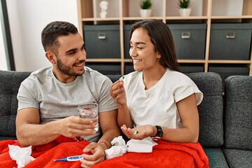 Fototapeta premium Young latin ill couple eating pills sitting on the sofa at home.