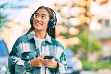 Young latin girl smiling happy using smartphone and headphones at the city.