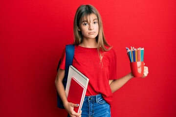 Teenager caucasian girl holding art notebooks and colored pencils depressed and worry for distress,...