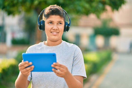 Adorable latin boy smiling happy using headphones and touchpad at the park.