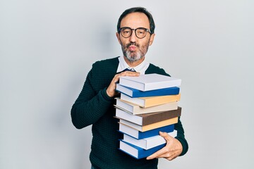 Middle age hispanic man holding a pile of books looking at the camera blowing a kiss being lovely and sexy. love expression.