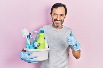 Middle age hispanic man holding cleaning products smiling happy and positive, thumb up doing excellent and approval sign