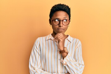 Young african american girl wearing casual clothes and glasses thinking concentrated about doubt with finger on chin and looking up wondering