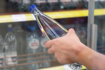 Man holds in his hand a plastic bottle with pure mineral water on the background of a shop window.