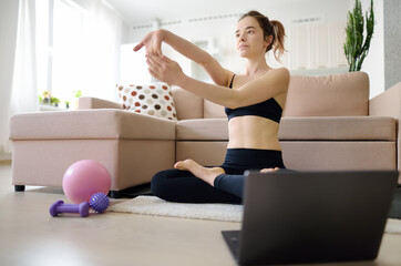 Distance sport fitness training workout. Young woman does yoga or stretching online using a laptop at home. Entertainment, training, education and sports via the Internet.