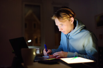 Fototapeta premium Shocked teenger studying night at home with laptop and tablet pc. Online learning, distance lessons, freelance - modern lifestyle