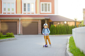 Little child in safety helmet riding scooter to school. Preschooler boy waving hand saying hi. Safety kids by way to school.