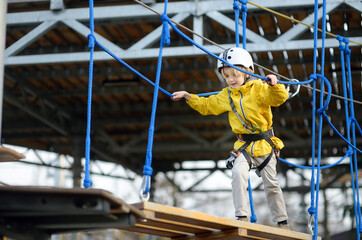 Little boy having fun in Adventure Park for children amoung ropes, stairs, bridges. Outdoor climbing adventure playground in public park. Activity entertainment for kids