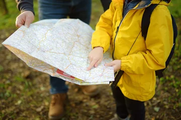 Fotobehang Schoolchild and his mature father hiking together and exploring nature. Little boy with dad looking map during orienteering in forest. Adventure, scouting and hiking tourism for kids. © Maria Sbytova