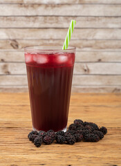 Blackberry juice in a glass with ice and fruits over wooden table