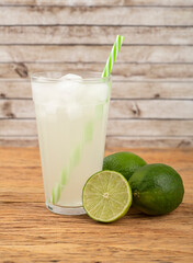 Green lemon juice in a glass with ice and fruits over wooden table