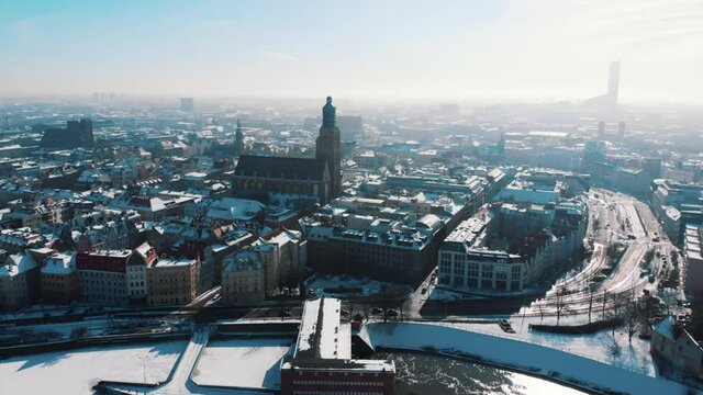 Drone footage of the city of Wroclaw, Poland. Busy street with vehicles moving. St. Mary Magdalene and Elisabeth Churches can be seen from a distance. Snow-covered street. 
