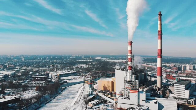 Drone footage of smoke coming out from the chimney of a thermal power plant in the industrial area of Wroclaw, Poland. Harmful smoke polluting the beautiful blue sky. City skyline. 