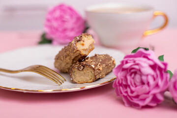 Golden colored eclairs on plate with fork and cup of tea, on pink background