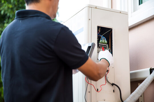 Close up technician hand using measuring equipment checking electric current voltage at circuit breaker on outdoor air compressor unit after installation and air conditioner services maintenance