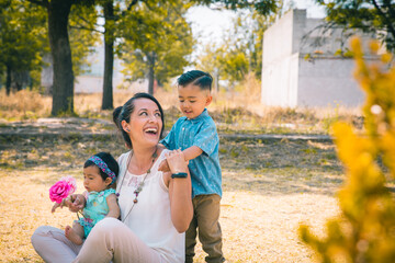 Mamá mexicana con sus hijos jugando en un parque felices 