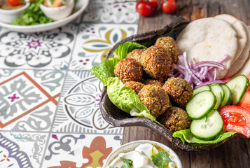 Falafel, fresh vegetables and pita bread on clay plate, gray background