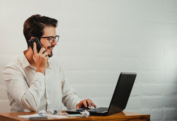 Latin man in glasses working. Using laptop and cell phone. Work at home concept. Copy space.