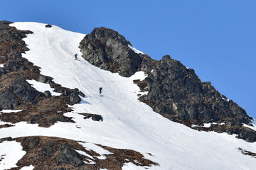 Fototapeta na wymiar Skiers make their way down a snow covered mountain in Alaska's Talkeetna Range.