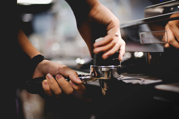 Barista presses ground coffee using tamper. Close-up view on hands
