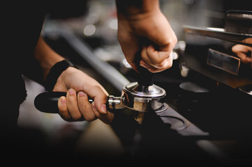 Barista presses ground coffee using tamper. Close-up view on hands