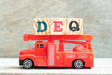 Fire ladder truck hold letter block in word DEQ (Abbreviation of Delivered Ex Quay) on wood background