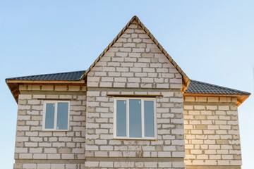 Building a house from foamed concrete blocks. Seams, raw facade. Roof of complex shape with a metal coating. Window. Background - blue sky.