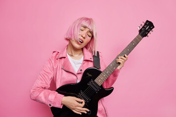 Obraz na płótnie Canvas Carefree female musician tilts head sings favorite song plays electric guitar performs on stage being popular rock star jas trendy pink hair poses indoor. Music lifestyle show business concept