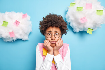 Sad disappointed young African American woman poses against blue background with pasted note cards...