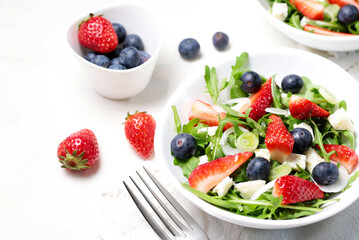 Insalata sana con fragole, mirtilli, rucola e formaggio feta sul piatto bianco.