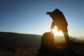 A photographer standing on a rocky tail holding a telephoto camera in the morning on the top of a mountain