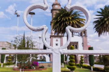 Fototapeta premium Old Mexican church, bushes, and palm trees from behind white fence
