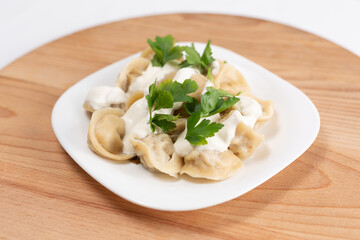 Dumplings with sour cream and herbs on a wooden background