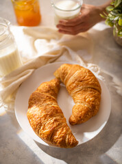 Breakfast in the morning. Morning light, two croissants, orange jam, milk. Hands of the girl at breakfast. Hospitality business. Breakfast in french style.