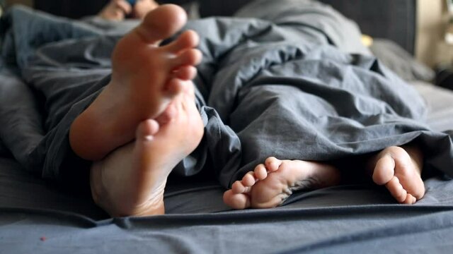 couple legs woman and man under the grey blanket in bed