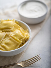 Homemade Italian ravioli or dumplings, Russian pelmeni.Dumplings with filling.with sour cream on a light background with space
