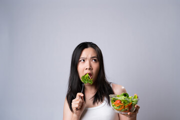 Fototapeta premium Asian woman confused with eating salad isolated over white background.