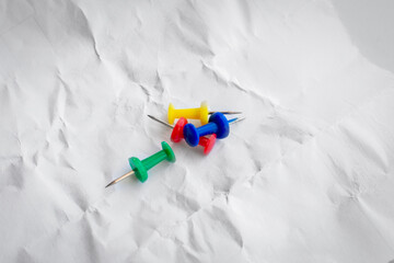 Multi-colored push pins lie on a sheet of crumpled, wrinkled paper. Close-up, top view.