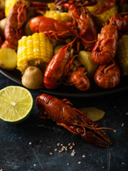 Boiled crayfish with potatoes and corn. With lemon and lime. On a dark blue table. Various recipes and recipe book