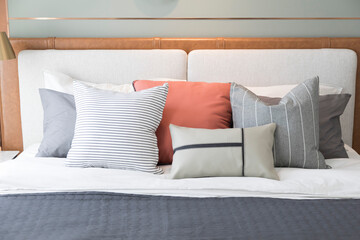Stylish interior of modern bedroom. White, grey and pastel orange design pillow setting in cozy bedroom with clock on the wall.