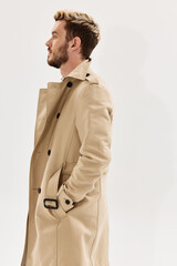 man holding hands in pockets of beige coat side view light background