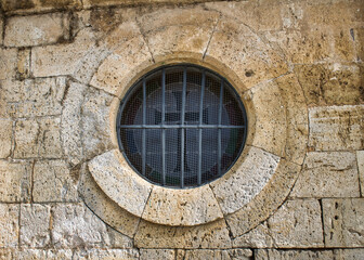 Ventana circular con barrotes de hierro en muro de piedra de la iglesia Santiago apóstol de Villalba de los Alcores, provincia de Valladolid, de estilo románico