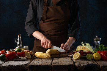 The cooking chef cuts the corn to make a dish with crayfish and potatoes. Recipe book and cooking